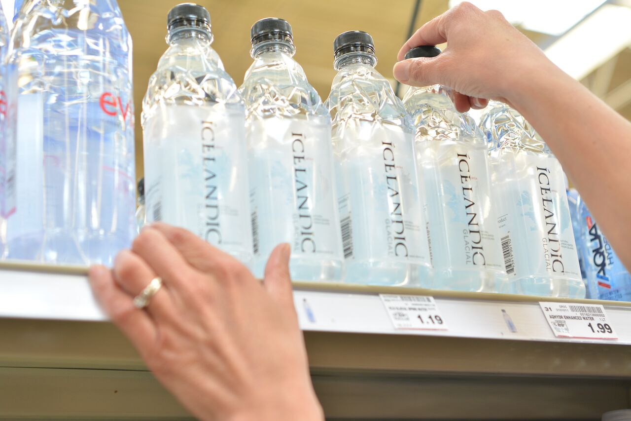 person touching bottle of water on top shelf